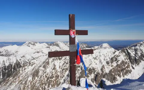 Drewniany krzyż z flagą Słowacji na szczycie Kriváň, narodowej góry Słowaków, na tle ośnieżonych Tatr.