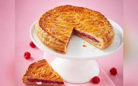 Galette framboise dorée sur un présentoir blanc, une part coupée révèle la garniture rose. Parfait pour une recette galette framboise.