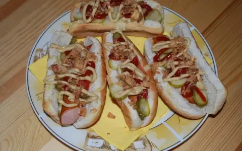 Cztery pyszne domowe hot dogi z kiełbaską, ogórkiem, ketchupem, musztardą i chrupiącą cebulką na talerzu.