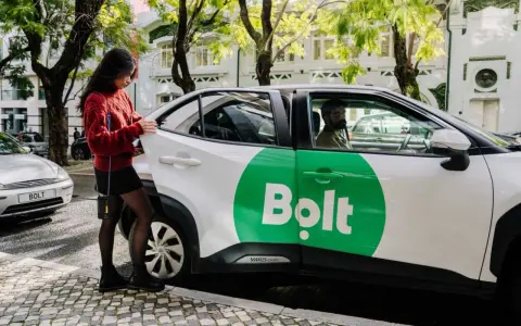 Junge Frau öffnet Tür eines weißen Bolt-Taxis. Fahrer wartet.