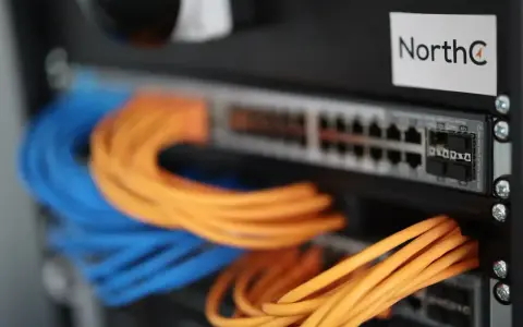Netzwerkschrank mit blauen und orangen Kabeln, die an einen Switch angeschlossen sind.