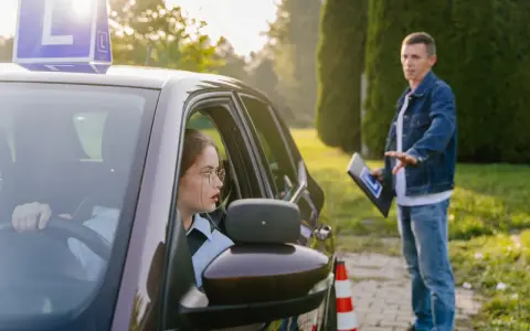 Młoda kobieta w okularach uczy się jeździć, a instruktor pokazuje jej, ile ważny jest kurs prawa jazdy.