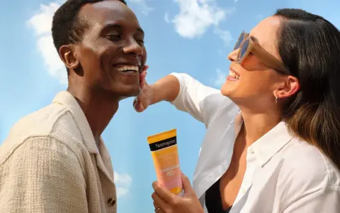 Un homme rit sous le soleil, une femme lui applique de la crème solaire pour protéger son visage.