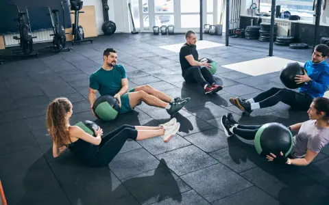 Fünf Personen machen im Fitnessstudio Sit-ups mit Medizinbällen.