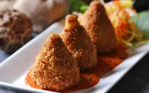 Złociste arancini, idealne do domowego arancini przepis, podane na talerzu z sosem pomidorowym i surówką.