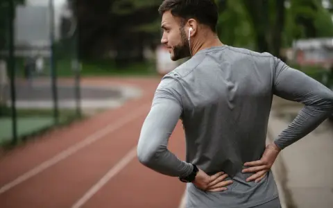Uomo con le mani sulla schiena, che indica dolore. Forse correre fa male alla schiena, o forse è solo un momento di pausa.