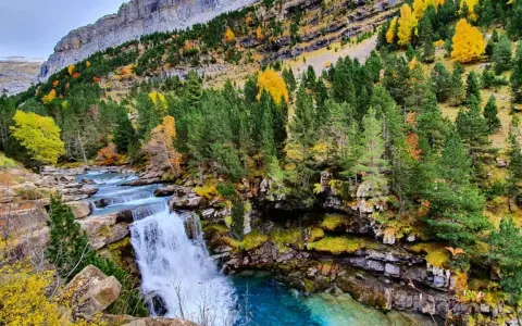 Cascada en un bosque otoñal de la cola de caballo huesca, con aguas turquesas y rocas cubiertas de musgo.