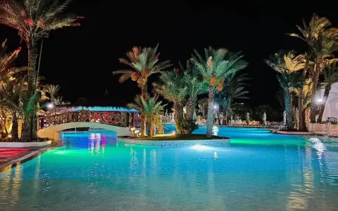 Nocny basen z palmami i mostkiem, idealne miejsce na relaks. Wiele pozytywnych fiesta beach djerba opinie potwierdza jego urok.