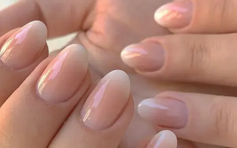 Delikatne, owalne paznokcie z subtelnym, perłowym połyskiem. Klasyczny francuski manicure w nowoczesnym wydaniu, podkreślający naturalne piękno dłoni.