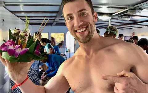 Smiling man on a boat in Asia, holding a flower offering. A perfect moment for gay travel in Asia.