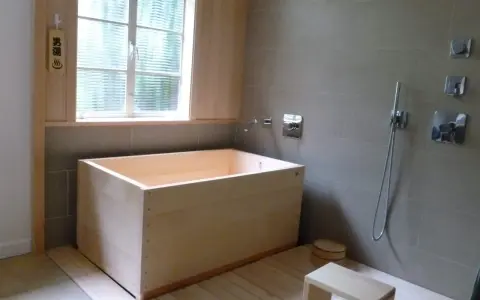 Un baño japonés con tina de madera, ducha y un pequeño taburete. El letrero de madera indica "男湯" (baño de hombres).