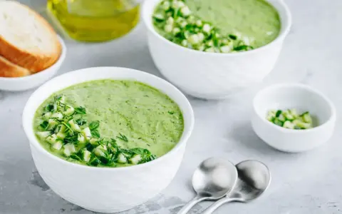 Deux bols de gaspacho concombre frais, garni de dés de concombre et d'herbes. Du pain grillé et de l'huile d'olive à proximité.