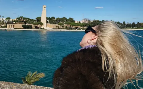 Kobieta z blond włosami podziwia pomnik i morze w Brindisi. Warto zobaczyć to miejsce!