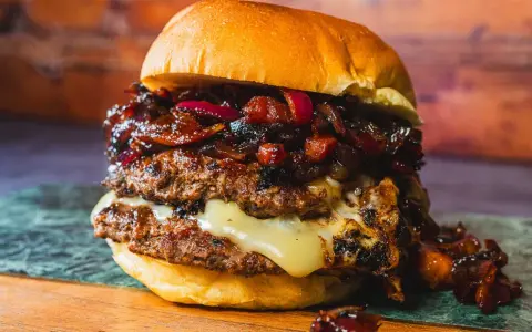 Saftiger Burger mit doppeltem Patty, geschmolzenem Käse und einer süß-salzigen Bacon Jam-Schicht, garniert mit roten Zwiebeln.
