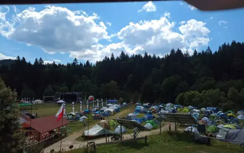 Pole namiotowe na festiwalu w Solinie. Tysiące namiotów pod błękitnym niebem z chmurami, w tle las i scena festiwalowa.