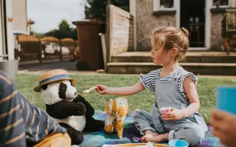 Dziewczynka karmi pluszową pandę na pikniku. Świetny sposób, co robić na nudę w ogrodzie!