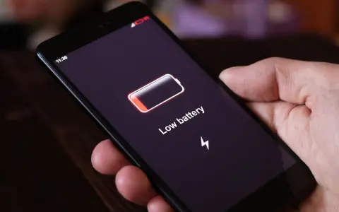 Dłoń trzyma smartfon z komunikatem "Low battery". Czas na naukę, jak oszczędzać baterię w telefonie, by uniknąć takich sytuacji.
