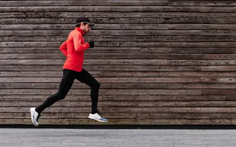 Ein Mann im roten Shirt und schwarzer Hose absolviert einen kraftvollen crescendo lauf vor einer rustikalen Holzfassade.
