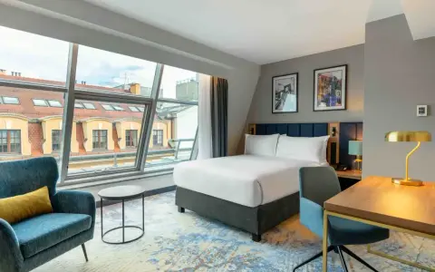 Nowoczesny pokój hotelowy z dużym oknem, łóżkiem i biurkiem. Czy trzeba być pełnoletnim, aby wynająć hotel? Tak, zazwyczaj tak.