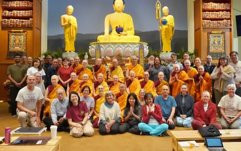 A large group of monks and laypeople gather for a photo in front of a golden Buddha statue, celebrating their shared religion.