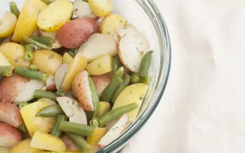 Insalata colorata di fagiolini e patate novelle, condita con erbe aromatiche, in una ciotola di vetro.