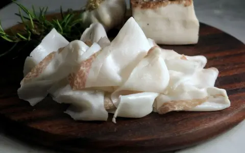 Fette sottili di lardo di Colonnata, profumate con rosmarino e aglio, pronte per essere gustate.