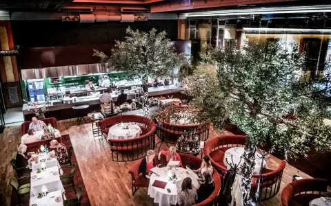 Elegant restaurang med runda, röda bås och träd. Köket syns i bakgrunden. Många gäster njuter av sin måltid. L'avventura recensioner verkar positiva.