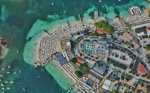 Albania najpiękniejsze miejsca: tętniący życiem kurort plażowy z białymi parasolami, turkusową wodą i basenami.