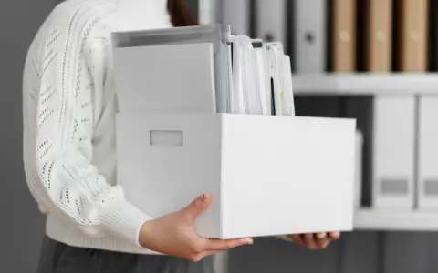 Osoba trzyma białe pudełko z dokumentami, ułatwiające przechowywanie dokumentacji pracowniczej.