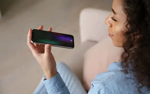 Kobieta trzyma telefon, na ekranie którego widać ikonę mikrofonu, sugerującą aplikację do nagrywania rozmów.