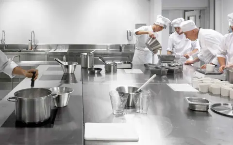 Estudiantes de cocina aprenden sobre seguridad en la cocina, preparando ingredientes en una estación de acero inoxidable.