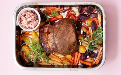 En saftig vildsvinsstek i ugn med rostade rotfrukter och en skål med lingonchutney.