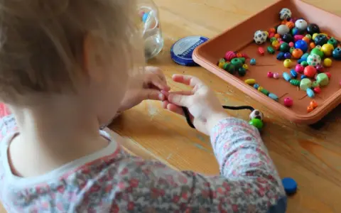 Dziecko uczy się, jak nawlec koraliki na sznurek, tworząc kolorową biżuterię.