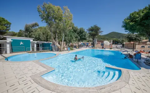 Dzieci pluskają się w basenie na terenie Miramare Camping Village. Słoneczny dzień, błękitne niebo i zieleń drzew tworzą wakacyjny klimat.