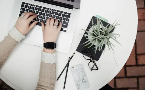 Kobieta pracuje na laptopie, obok leżą okulary, telefon i roślina. To idealne zdjęcia w chmurze do inspiracji.