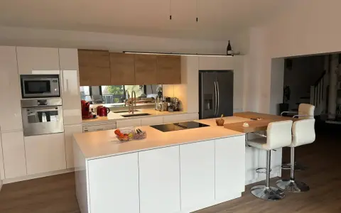 Cuisine moderne et lumineuse, avec îlot central. On y voit la différence entre une cuisine aménagée (meubles) et équipée (électroménager).