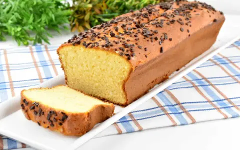 Puszysta babka z adwokatem, posypana czekoladową posypką, na białej paterze. Obok leży kromka ciasta.