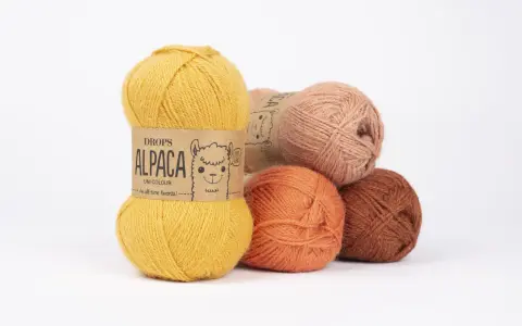 Garnnystan i varma färger som ockra, orange och rost. En guldig nystan från Drops Alpaca har en söt alpacka på etiketten.
