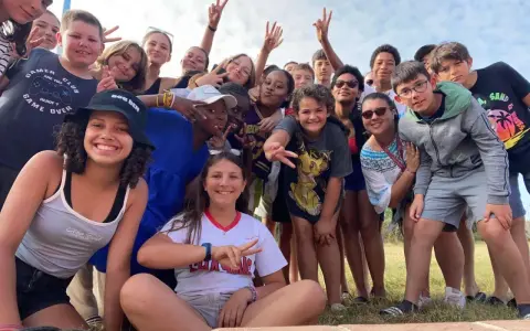 Un groupe d'enfants souriants fait un selfie en plein air, certains faisant le signe de paix.