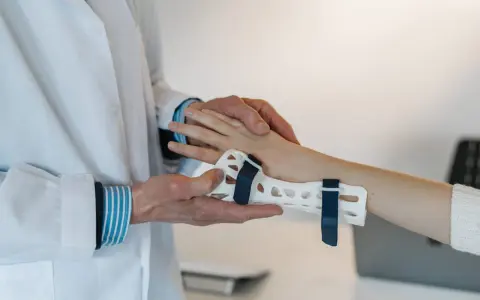 Lekarz zakłada pacjentowi ortezę na nadgarstek, co jest częścią terapii przy cieśni nadgarstka. Ćwiczenia pomogą w rehabilitacji.