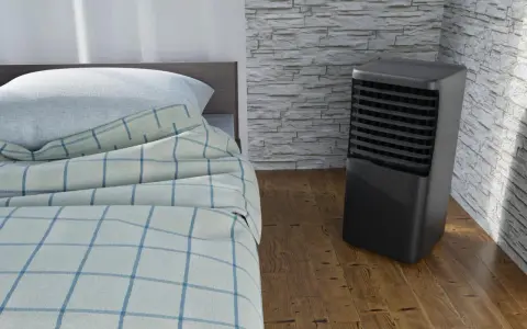 Un aire acondicionado portátil junto a una cama con sábanas a cuadros. ¿Qué es mejor, aire acondicionado portátil o fijo?