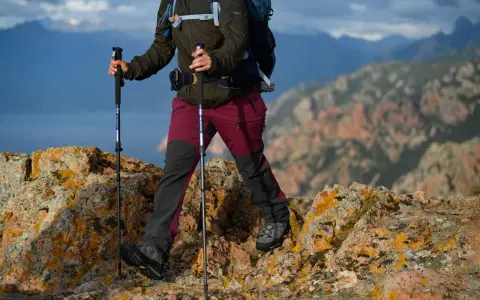 Osoba z plecakiem idzie po skalistym szlaku, używając kijków trekkingowych. Dobre kijki w góry to podstawa bezpiecznej wędrówki.