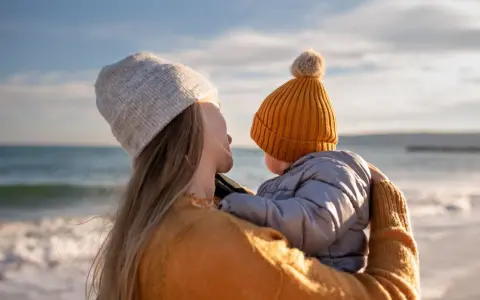 Madre abraza a su bebé en la playa, disfrutando de un momento de paz. Un respiro merecido, como una excedencia y vacaciones no disfrutadas, antes de volver a la rutina.