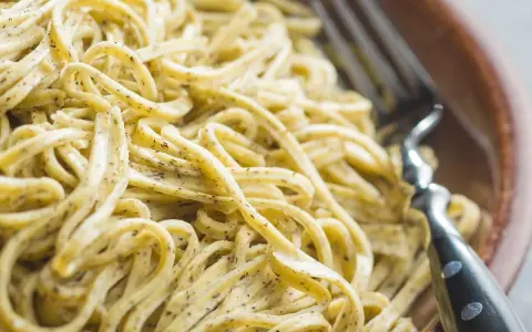 Un primo piatto invitante di tagliolini al limone, conditi con una salsa cremosa e profumata, pronti per essere gustati con una forchetta.