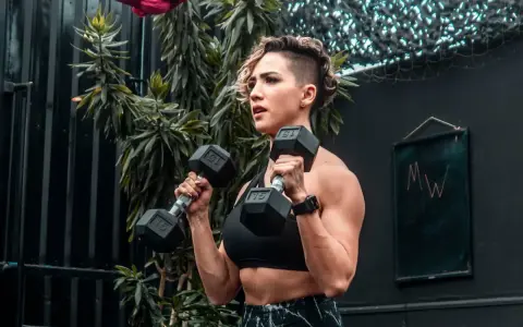 Kvinna utför hammer curls med hantlar. Stark och fokuserad, redo för nästa repetition.