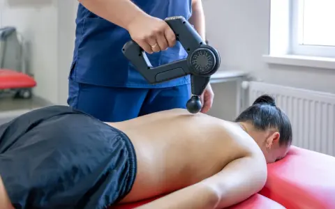 Fizjoterapeuta wykonuje masaż wibracyjny pleców. Choć zazwyczaj przynosi ulgę, warto pamiętać o potencjalnych skutkach ubocznych masażu wibracyjnego.