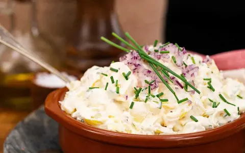 En krämig egen potatissallad med rödlök och gräslök, redo att serveras.