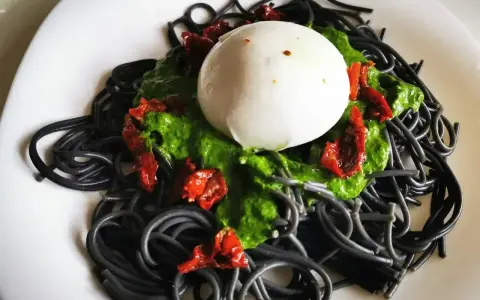 Czarny makaron z zielonym pesto, suszonymi pomidorami i kulką mozzarelli.
