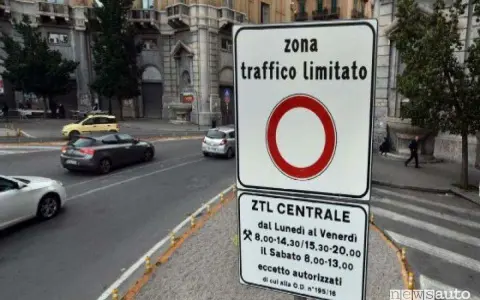 Cartello che indica "zona traffico limitato" con orari specifici. Auto in transito su strada urbana.