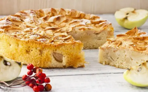 Un gâteau compote de pomme sans sucre, saupoudré de sucre glace, avec des quartiers de pomme et des baies rouges sur une table en bois.